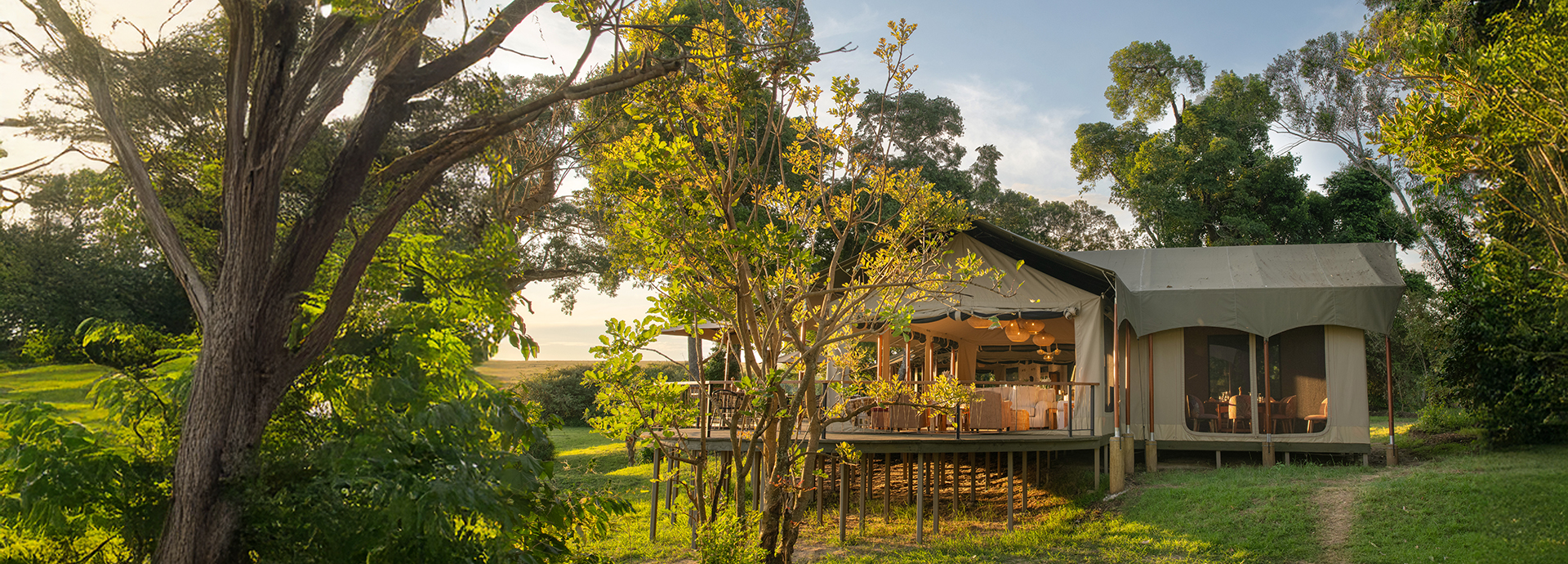 Side exterior of Rekero’s main tented area, set among open grassy glades and trees.