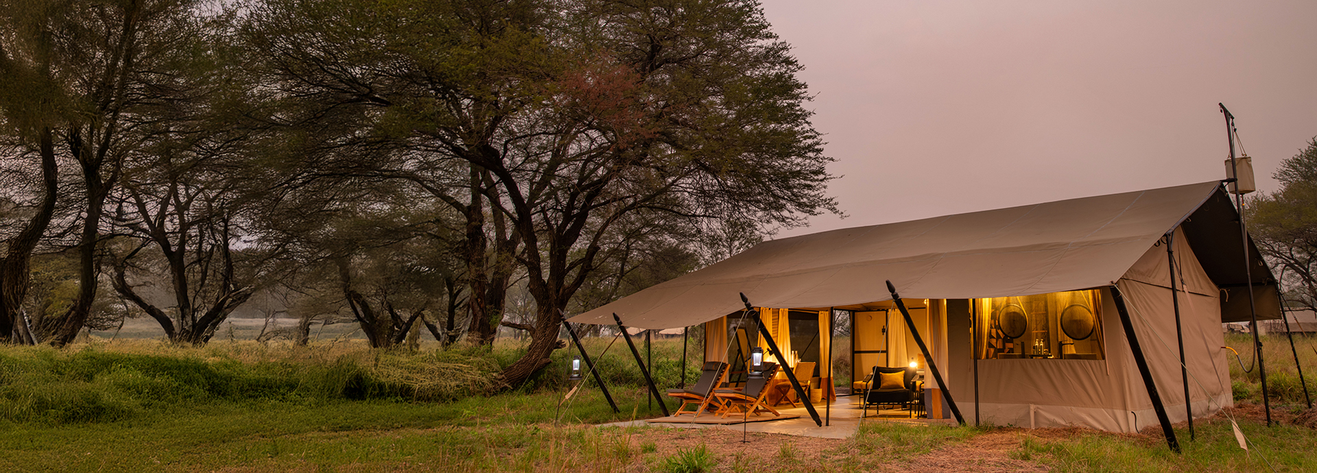 Guest tent at dusk with glowing lantern light under a pink-hued sky
