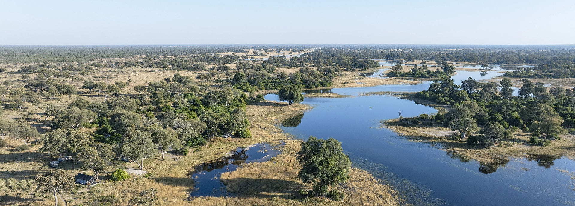 Aerial perspective of the Okavango Delta waterways surrounding the tents of Kweene River Camp.
