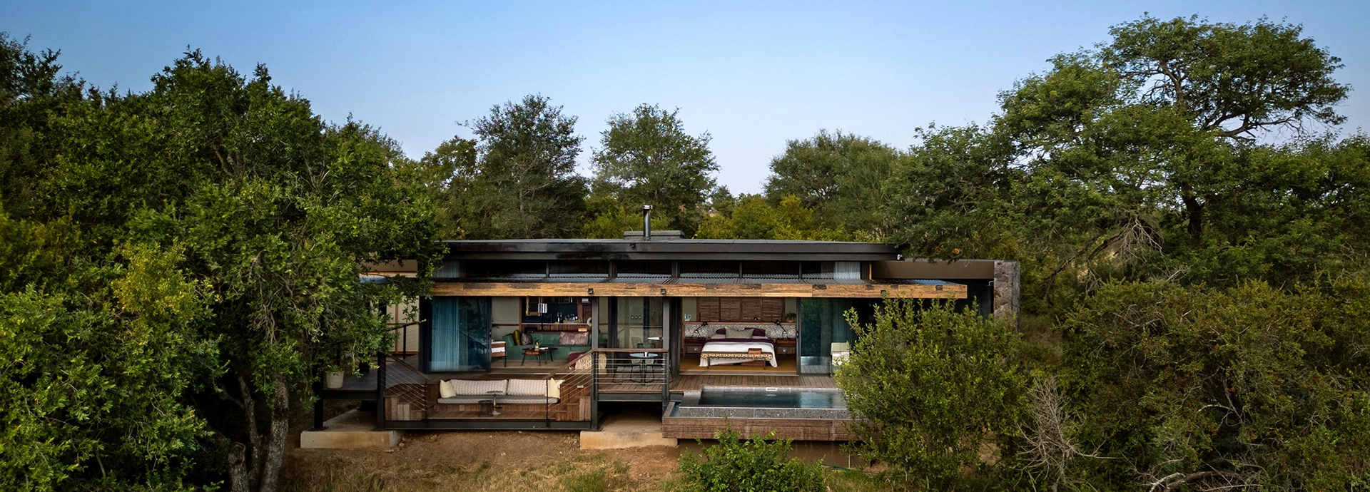 Exterior view of a Tanda Tula glass-and-canvas suite featuring a private deck and plunge pool surrounded by trees.