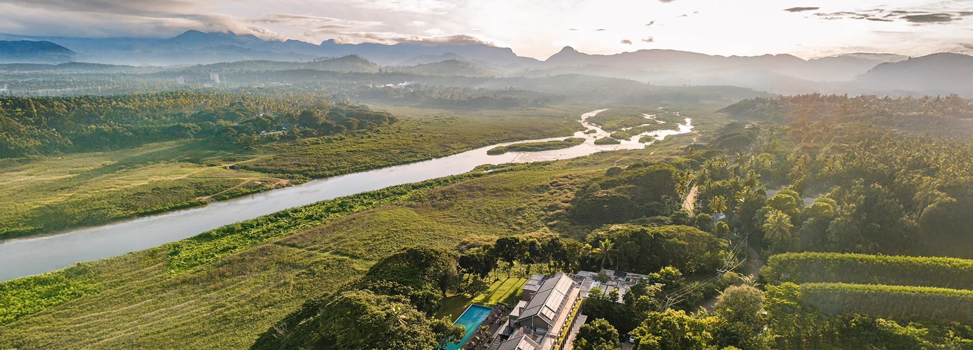 A sweeping aerial panorama captures Jetwing Kandy Gallery framed by lush wetlands, winding waterways and distant misty mountains.