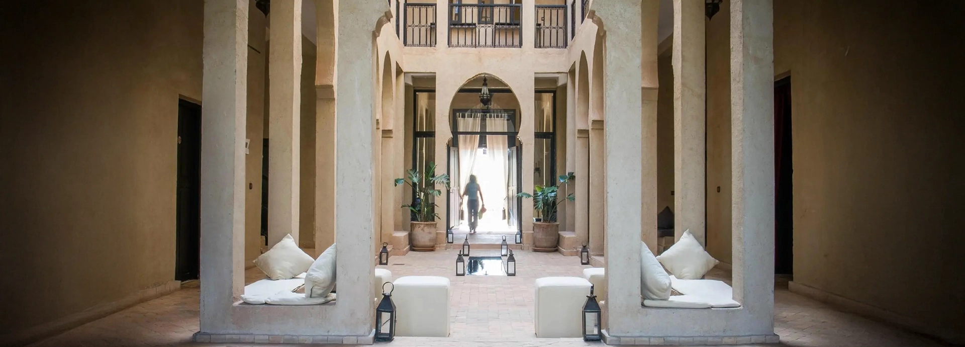 Bright courtyard with tall arches, tiled floor, and decorative lanterns beside a reflecting pool.