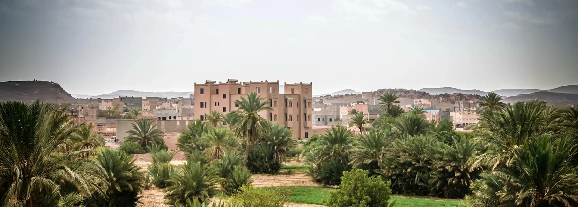 Exterior view of Dar Chamaa surrounded by palm groves with the Atlas foothills beyond.