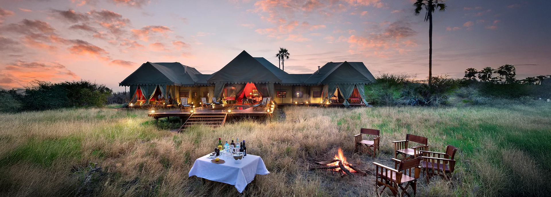 Guests enjoy a sundowner served by a guide on the shimmering salt pans against a vivid sunset.