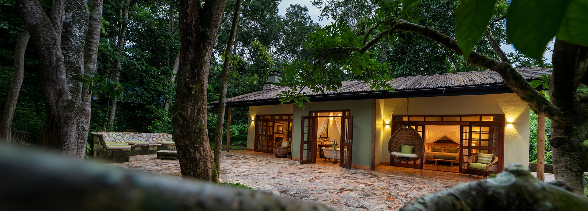 Honeymoon Cottage at Primate Lodge with soft lighting and open doors leading into the rainforest surroundings in Kibale, Uganda.