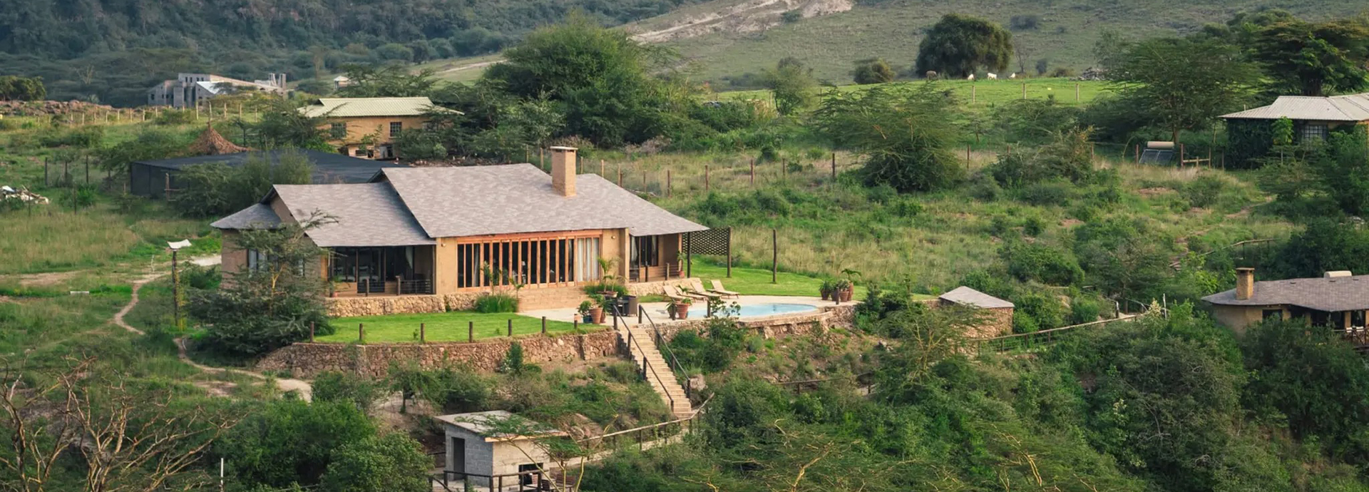 A luxury lodge building with a pool is set against a backdrop of lush green hills near Nairobi National Park.
