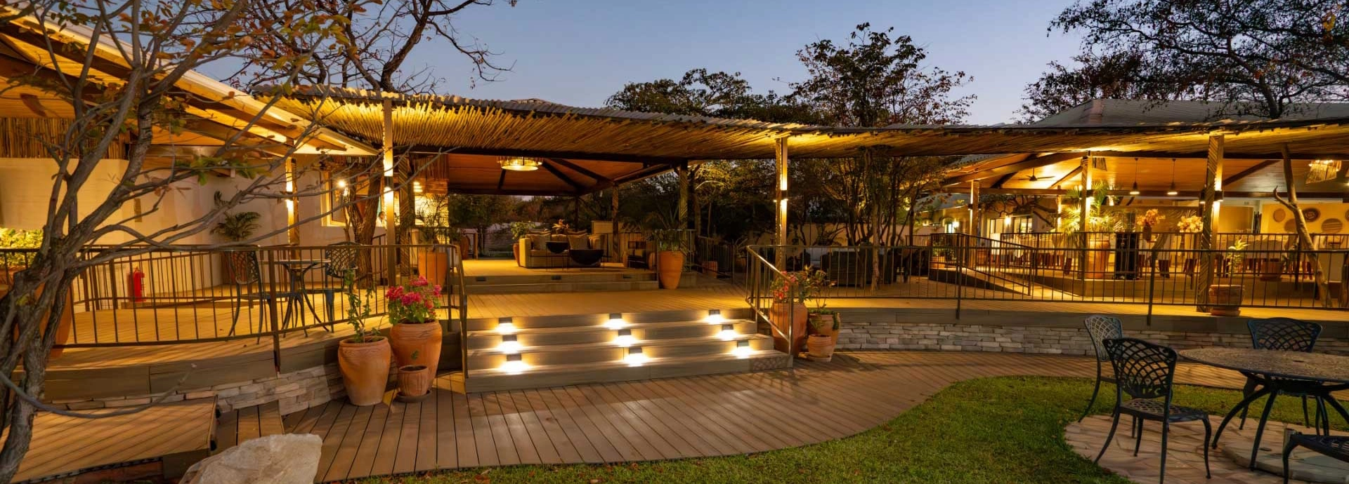 Warmly lit decked terrace with lounge and dining spaces beneath a thatched roof at Insika Lodge, Victoria Falls.
