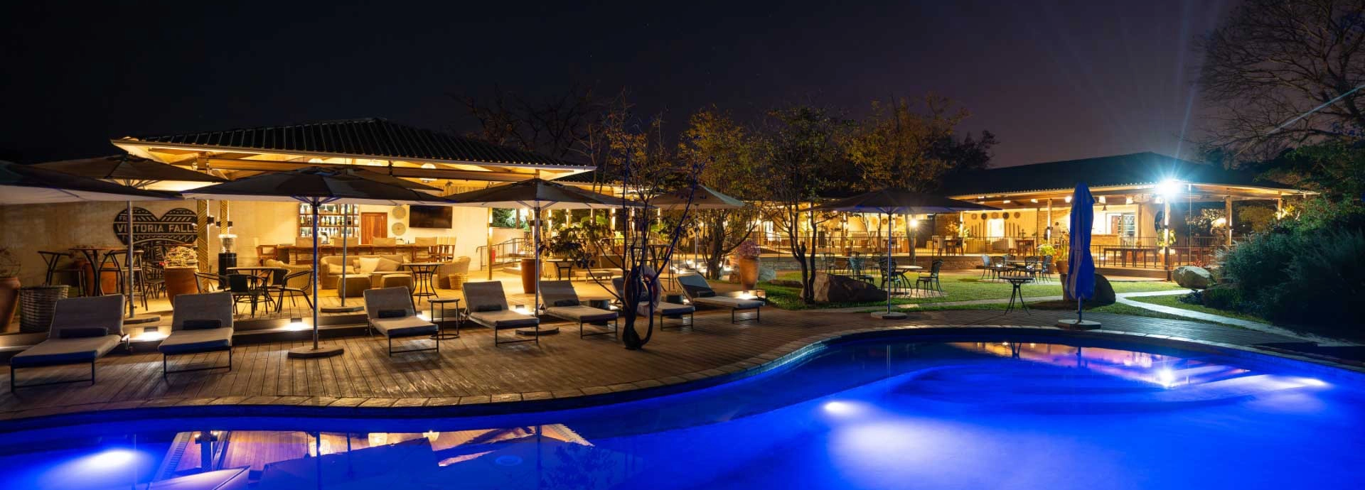 Pool deck illuminated at night with sun loungers and bar area at Insika Lodge, Victoria Falls.