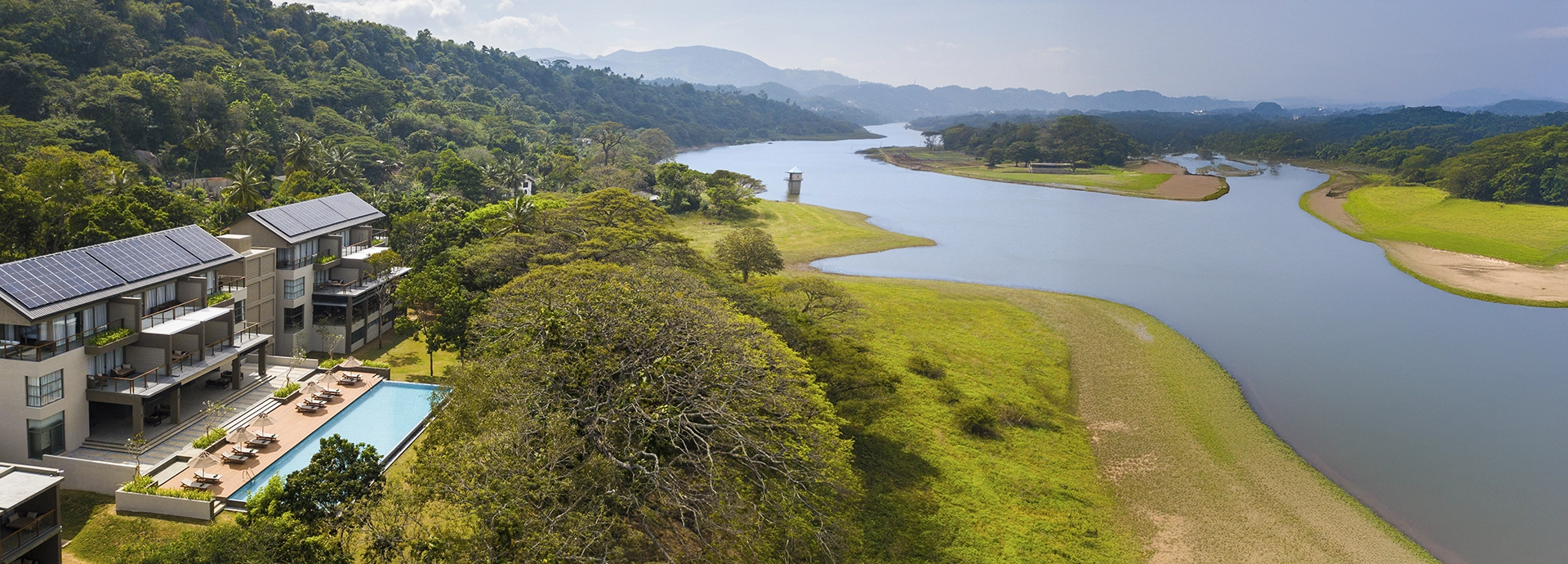 An elevated view of Jetwing Kandy Gallery shows its pool terrace overlooking the winding river and tree-clad hills of Kandy.