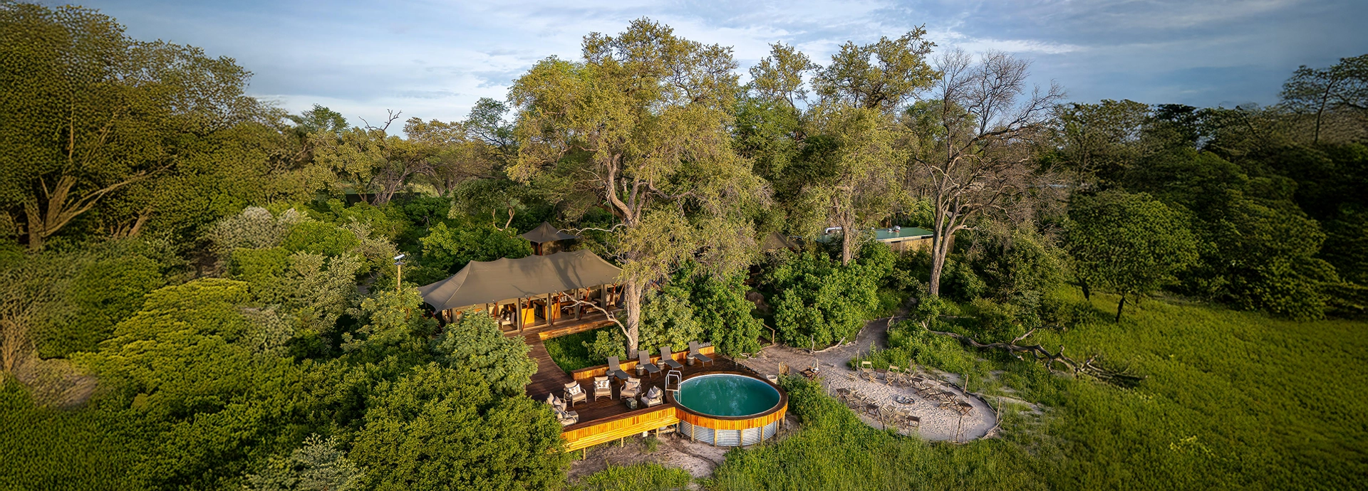 An aerial view reveals Karangoma’s tented camp shaded by mature trees with a circular pool overlooking green floodplains.