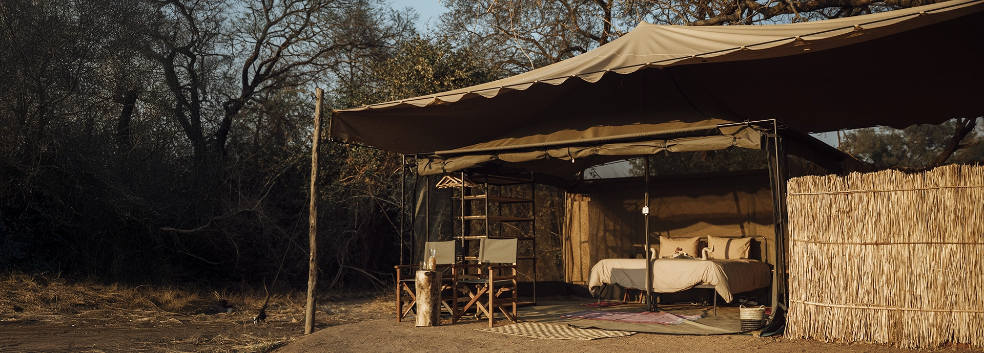 An open-fronted safari tent at Kutandala Camp with canvas awnings, outdoor seating and uninterrupted views into the surrounding bush.