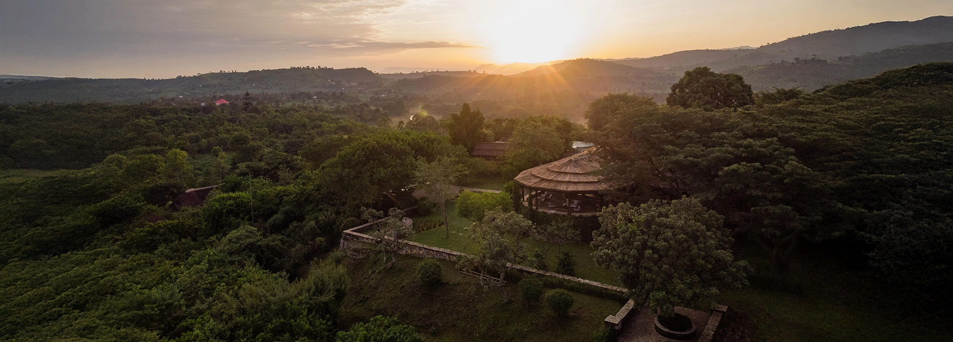 Sunset light washes over Kyambura Gorge Lodge, revealing its elevated position overlooking rolling green valleys and surrounding wilderness.