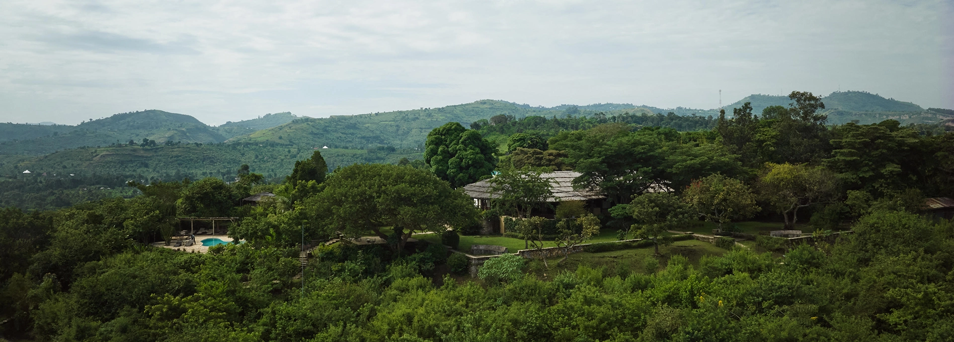 A wide aerial view of Kyambura Gorge Lodge set amid lush forested hills on the edge of Queen Elizabeth National Park in western Uganda.