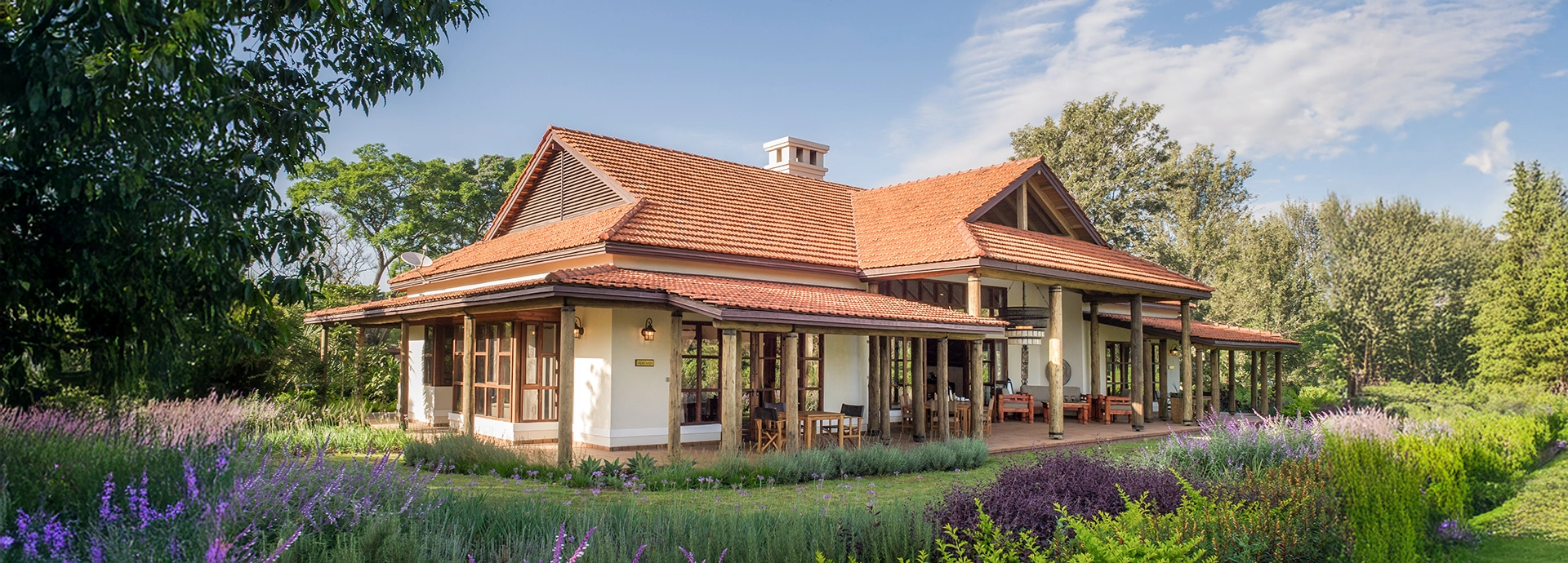 Exterior view of a family cottage at Legendary Lodge in Arusha, set among flowering gardens with wide verandas and classic East African architectural details.