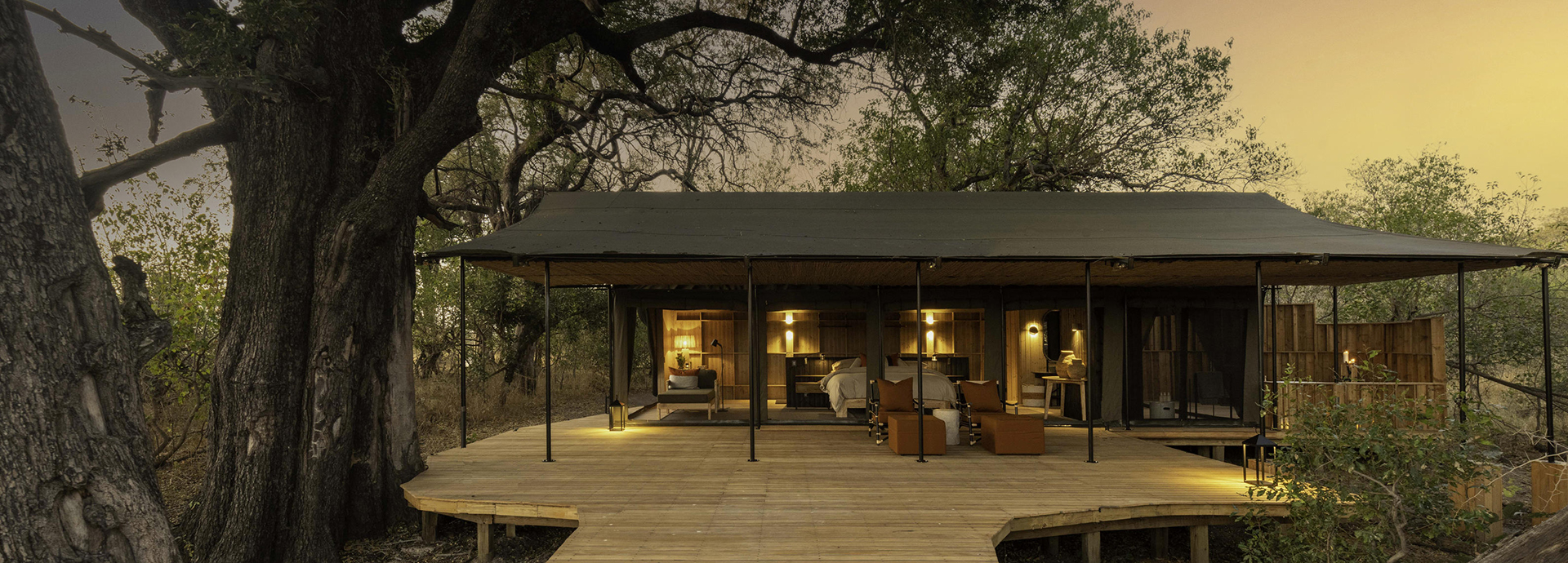 A spacious tented suite at Kiri Camp with wooden deck and glowing interior lighting at dusk.