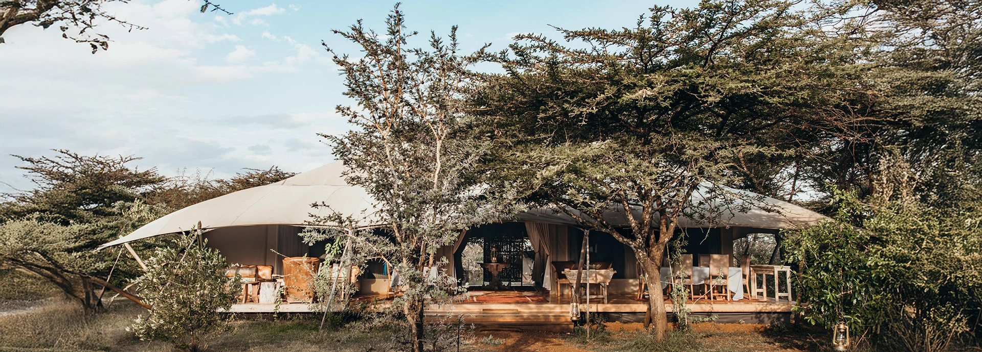The main guest area at Mara Expedition Camp in Kenya, set beneath sweeping canvas with open decks and relaxed seating surrounded by acacia woodland.
