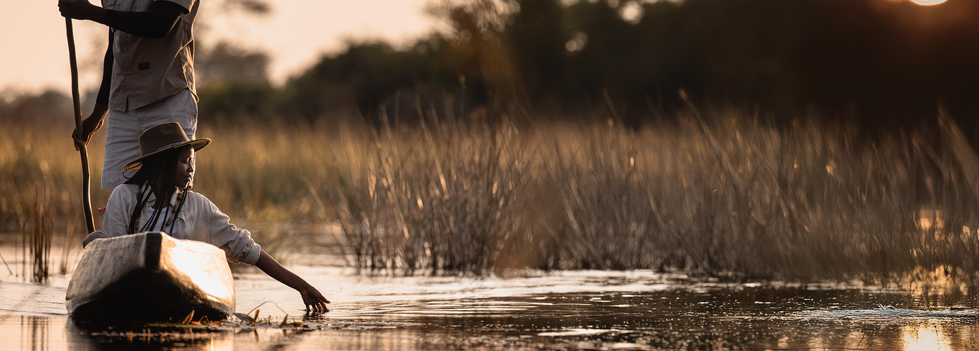 A guide poles a mokoro through the Delta’s waterways with a guest trailing her hand in the water.