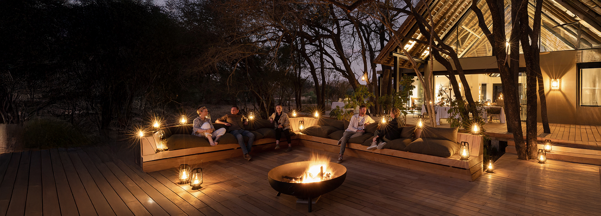 Evening dining setup with fire pit and lanterns, creating an intimate outdoor atmosphere beneath the trees.