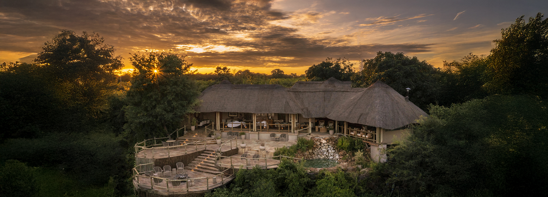 Ngoma Safari Lodge at dusk, showcasing its multi-level wooden decks and thatched roof surrounded by lush greenery.
