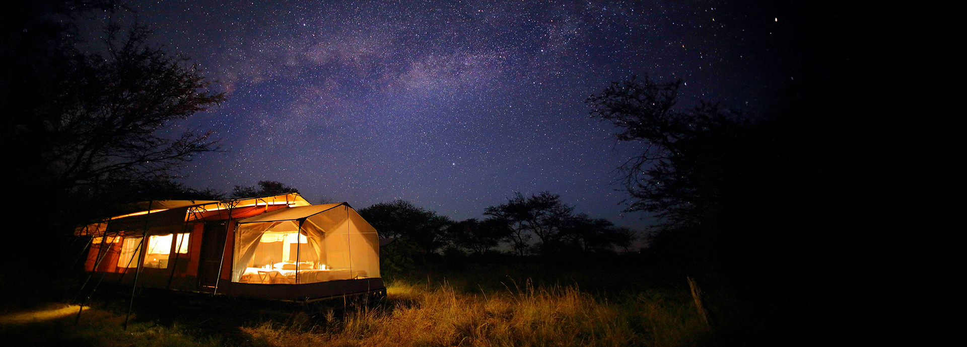 Stargazing tent at Olakira lit warmly under a blanket of stars in the Serengeti.