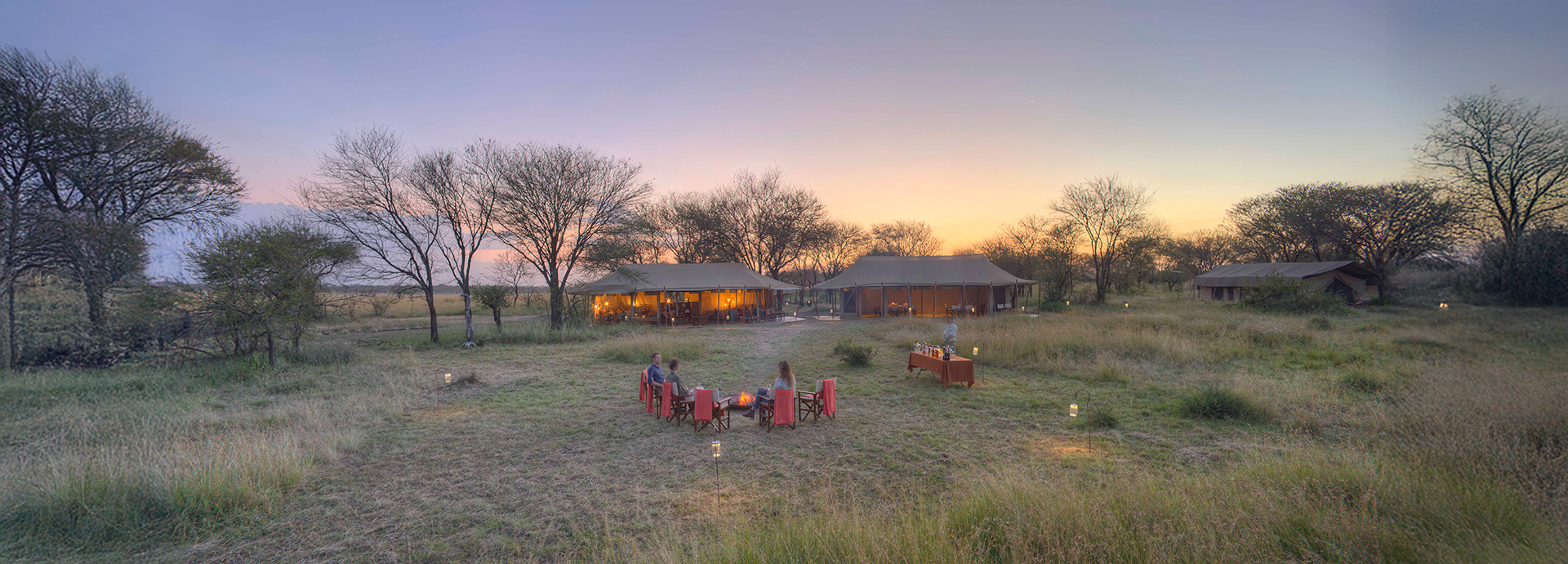 Guests enjoying sundowners around a firepit at Olakira Migration Camp as the sun sets.