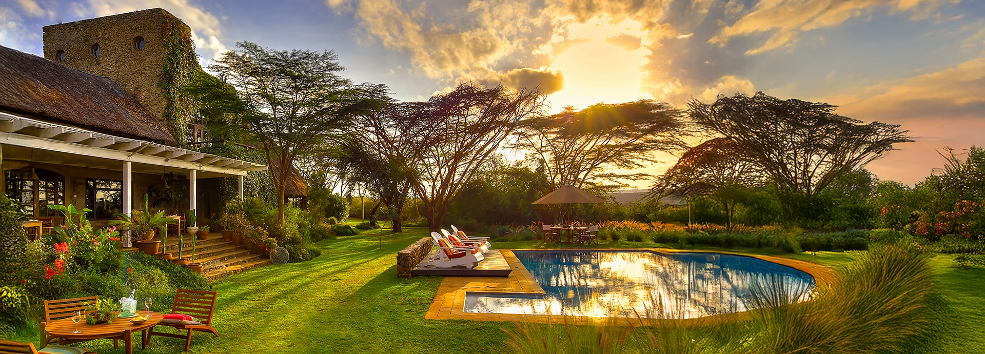 Golden sunset over Ololo Safari Lodge’s garden and swimming pool with acacia trees casting long shadows across the manicured lawn.