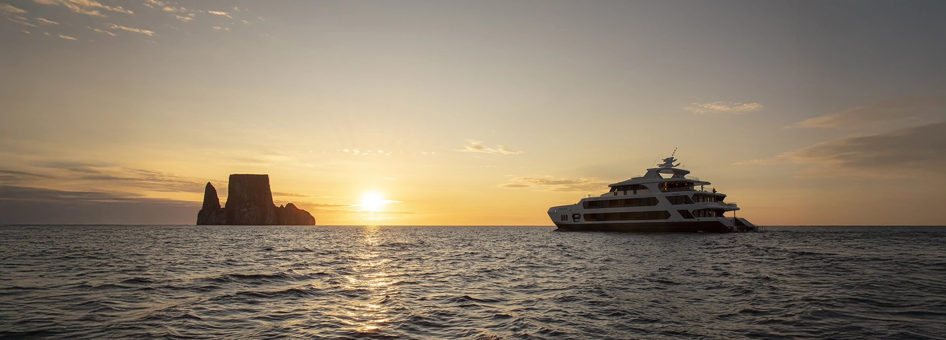 Hermes Galápagos Mega Catamaran sailing into golden evening light near Kicker Rock.