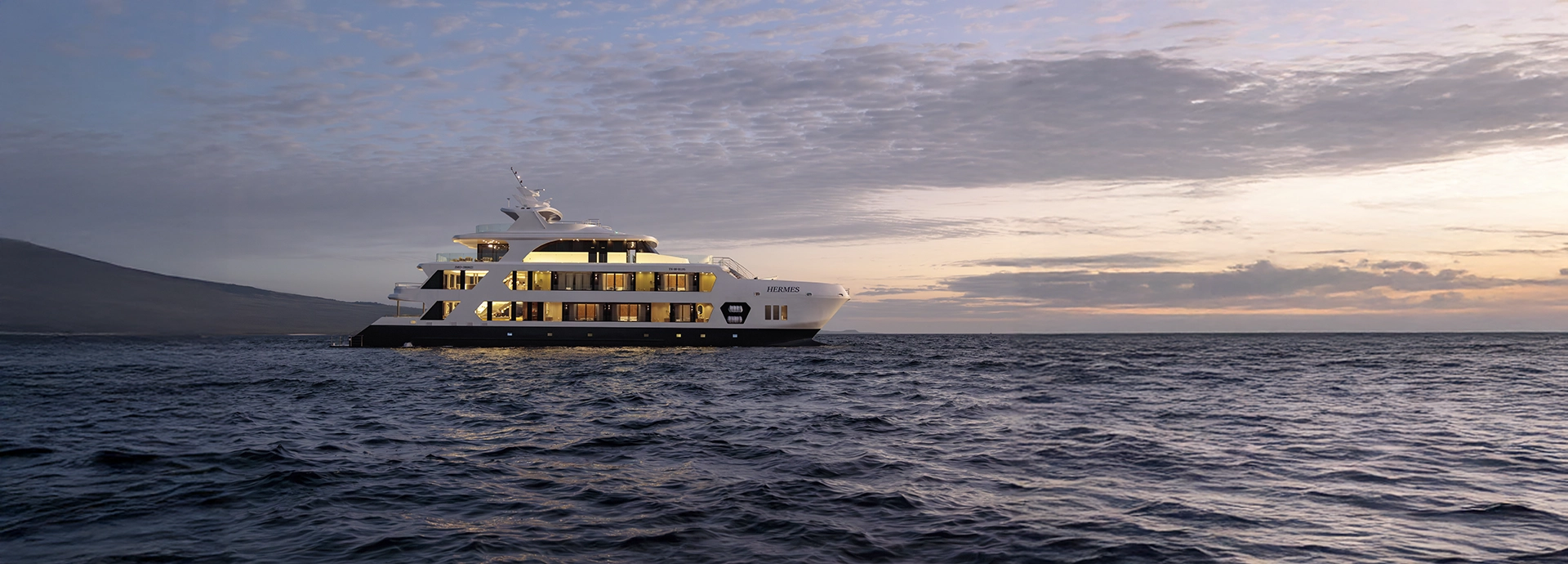 Hermes Galápagos Mega Catamaran cruising past volcanic cliffs at sunrise.