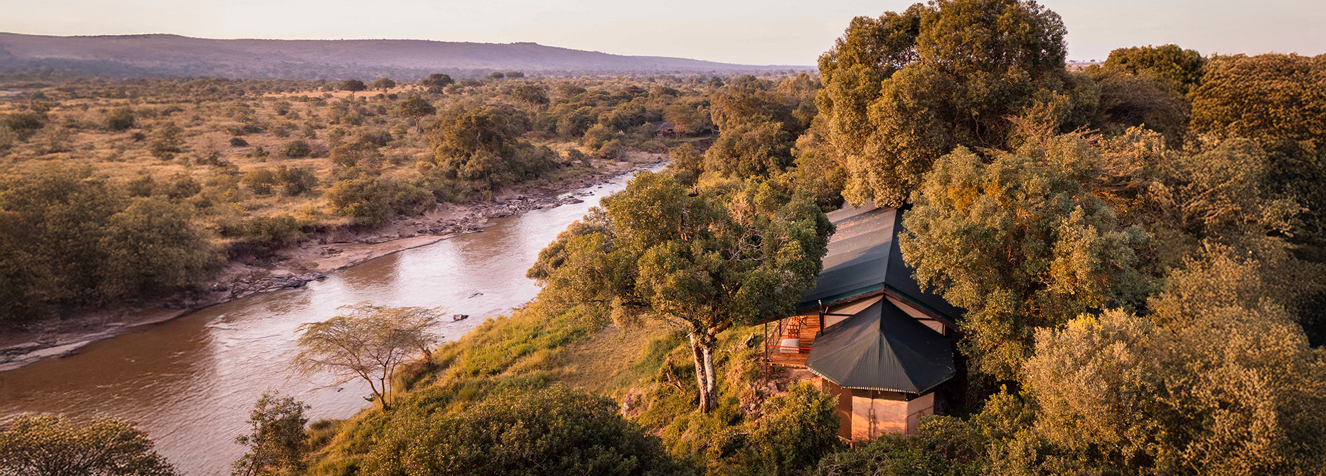 Aerial view of Serian ‘The Original’ perched beside the Mara River, with golden savannah stretching into the distance.