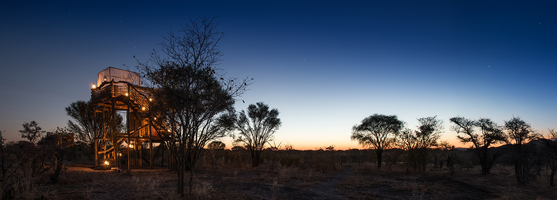 A Skybed platform lit by lanterns beneath a starry twilight sky, framed by trees.