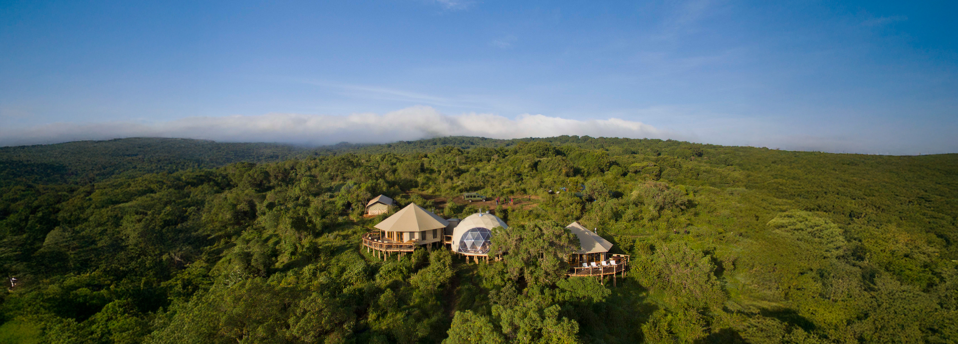 Aerial view of The Highlands camp surrounded by lush green forest and volcano slopes