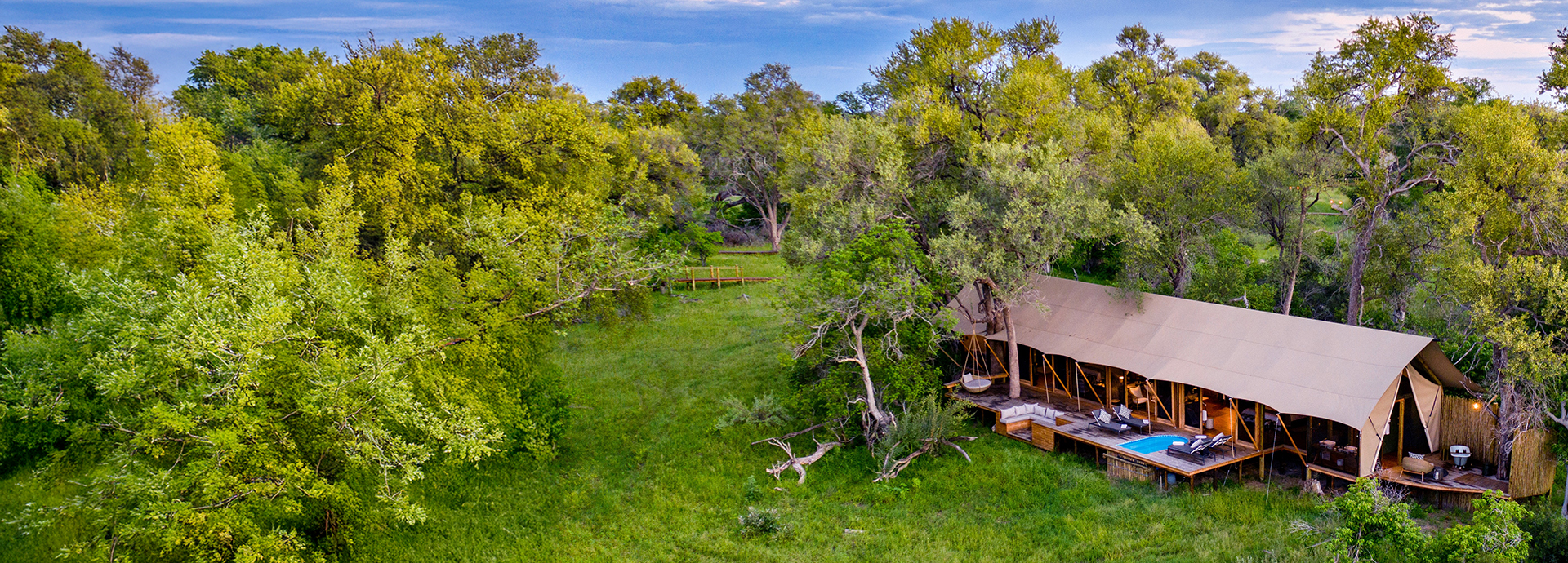 Wide-angle aerial view of Tuludi Camp’s family tent surrounded by dense green forest and open grassy clearings.