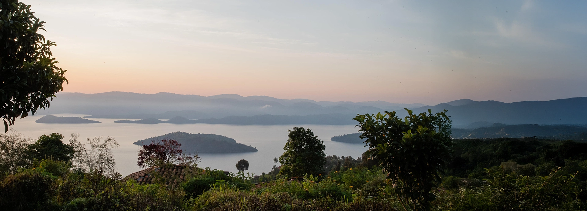 Early evening light settles over Lake Bulera as seen from Virunga Lodge, with calm waters, forested islands and layered hills creating a serene panorama.