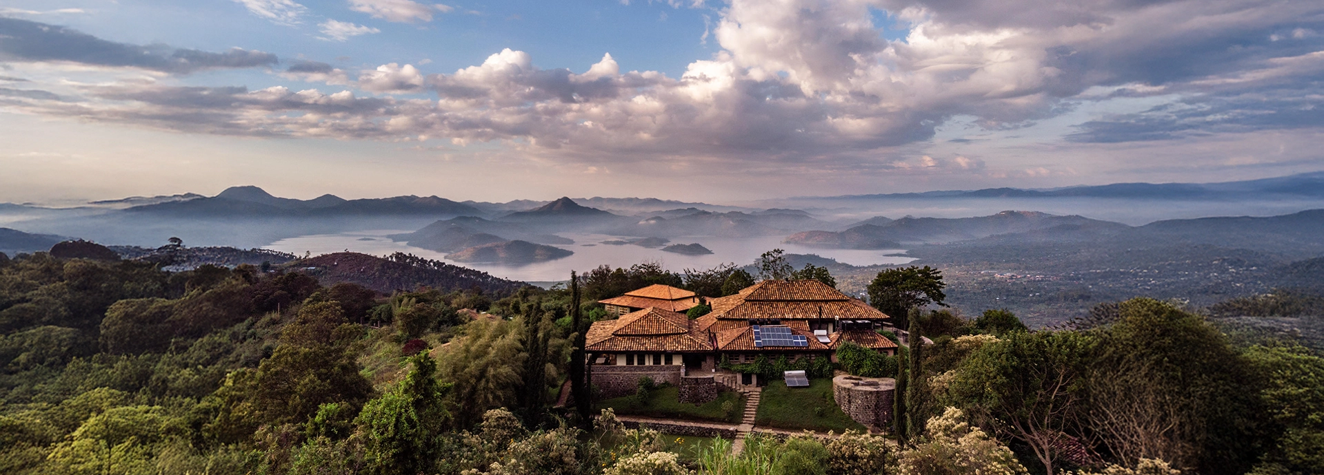 An aerial view of Virunga Lodge reveals its stone cottages perched high above Lakes Bulera and Ruhondo, surrounded by misty hills and layered volcanic landscapes.