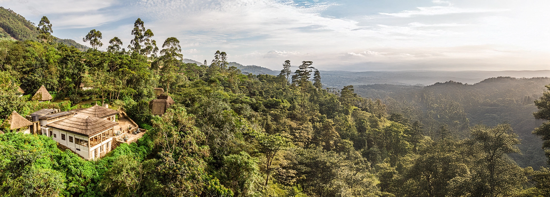 An elevated view of Volcanoes Bwindi Lodge tucked into the forested hills above Bwindi Impenetrable National Park, with sweeping green valleys stretching into the distance.