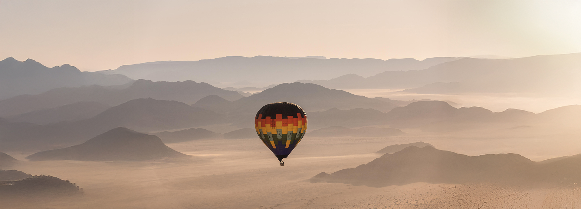 Hot-air balloon drifts across the Namibian Sossusvlei desert at sunrise