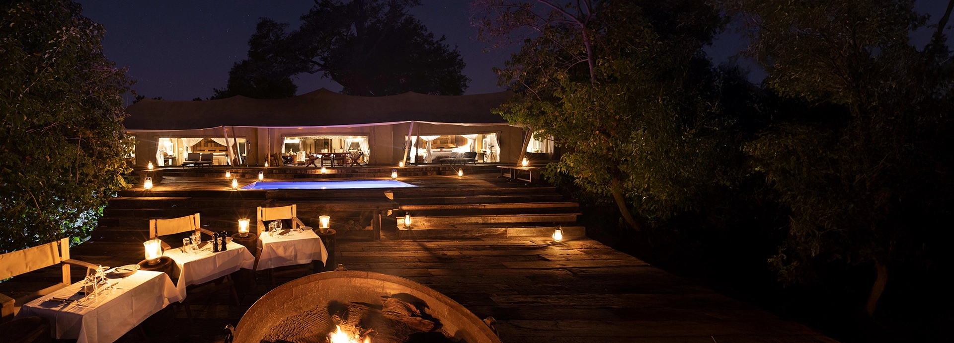 Evening dining at the Zarafa Dhow Suite in the Selinda Reserve, with candlelit tables set on a raised wooden deck overlooking the floodplains.