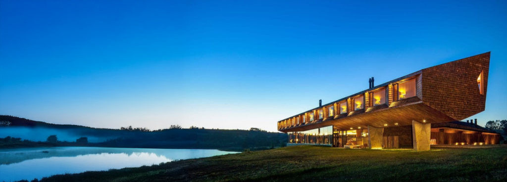 Coastal cliffs and a lone rock formation on a beach fringed with yellow flowers