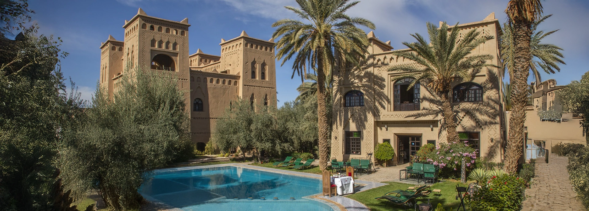 Inviting swimming pool surrounded by palm trees, sun loungers, and kasbah-style walls in the gardens of Ksar El Kabbaba.