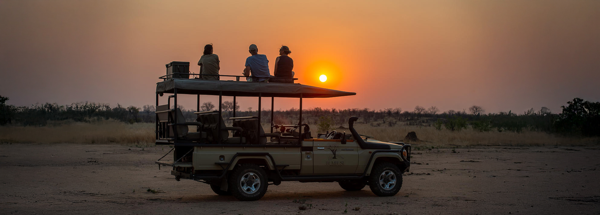 Safari game vehicle at sunset with guests and guide sitting on the roof