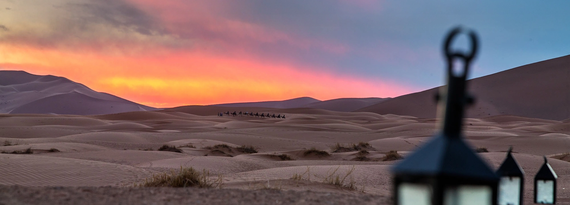 Expansive desert landscape with Riad Madu camp tents and dunes glowing in the morning light.