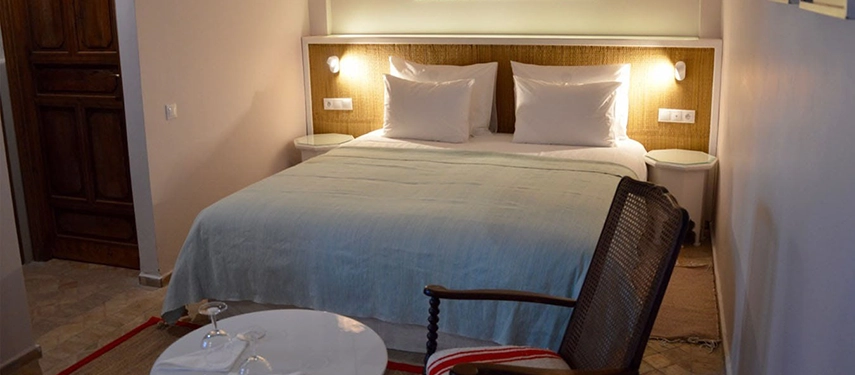 A cosy double bedroom with soft lighting, crisp white bedding, and a pale blue throw creating a warm and welcoming atmosphere.