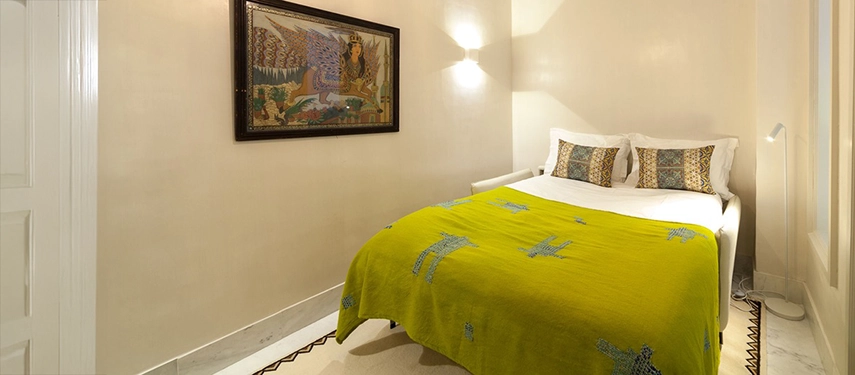 Cosy guest room with a bright green embroidered blanket, traditional artwork, and soft ambient lighting.