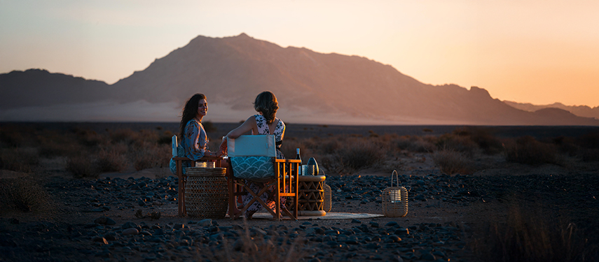 Tourist couple enjoy sundowners overlooking the desert at Kulala Desert Lodge, Namibia
