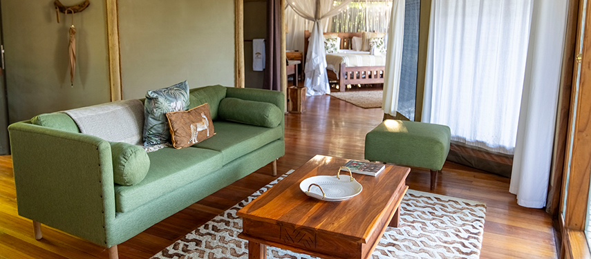 A stylish sitting area inside a luxury tent at Anabezi, with green furnishings and wooden finishes.