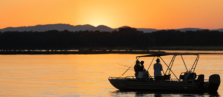 Guests enjoy catch-and-release fishing on a sunset boat cruise, silhouetted against glowing orange skies.
