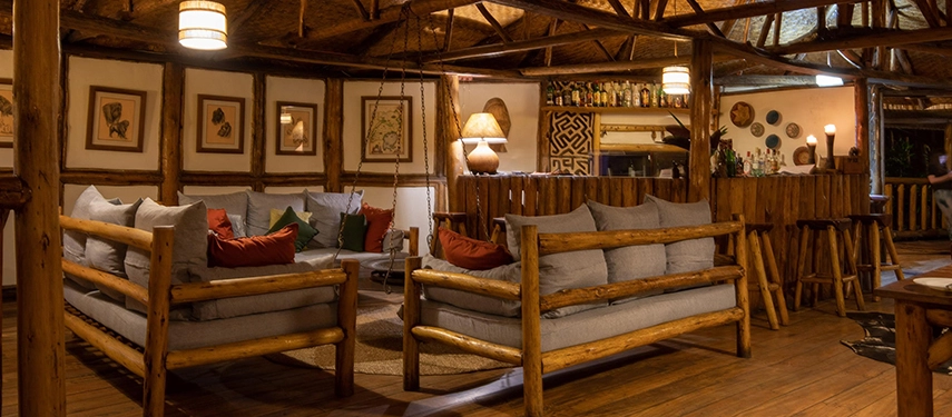 Warm wooden interior of Buhoma Lodge with rustic lounge seating & ambient lighting