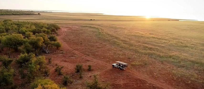 Aerial view of a safari vehicle travelling across open plains near Lake Kariba during late afternoon light.