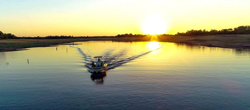Boat safari on Lake Kariba at sunrise, with calm water reflecting golden light as the vessel leaves a gentle wake behind it.