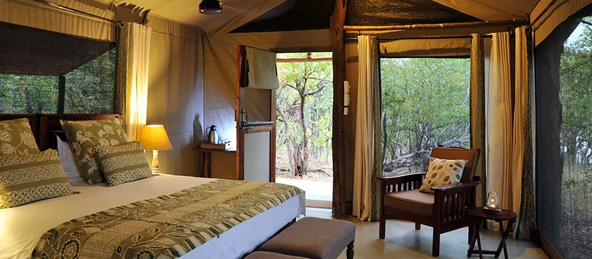 Elegant tented bedroom at Changa Safari Camp with soft lighting, natural textures, and open sides facing surrounding woodland.